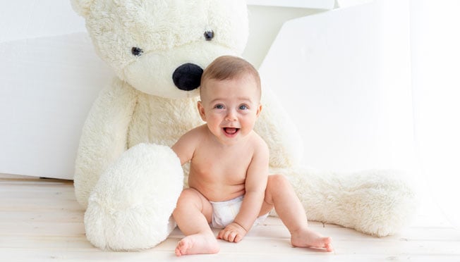 a baby boy in a diaper sitting next to a giant teddy bear